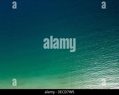 Hochwinkeldrohne aus türkisfarbenem und tiefblauem Meerwasser. Die Top-down-Perspektive zeigt natürliche Wellen und helle Sonnenlichtreflexionen auf dem Stockfoto