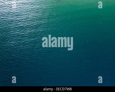 Hochwinkeldrohne aus türkisfarbenem und tiefblauem Meerwasser. Die Top-down-Perspektive zeigt natürliche Wellen und helle Sonnenlichtreflexionen auf dem Stockfoto
