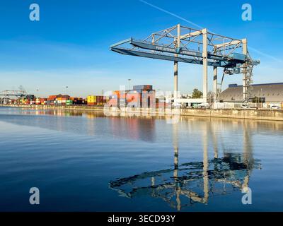 Straßburg, Frankreich - 11. April 2022: Schwerer Kran auf der Uferseite des städtischen Containerterminals am Rhein, mit Reflexion in stillen Gewässern. Stockfoto