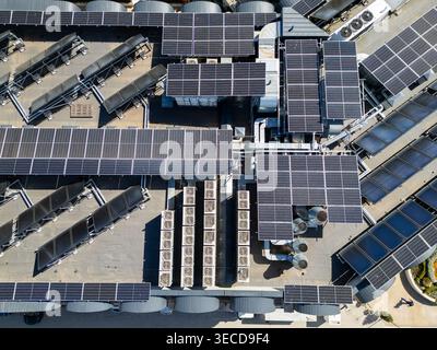 Hochwinklige Drohnenaufnahme einer großen Solarpaneel-Installation auf einem Flachdach. Dolly zoomt vorwärts und zeigt saubere Infrastruktur für erneuerbare Energien und Stockfoto