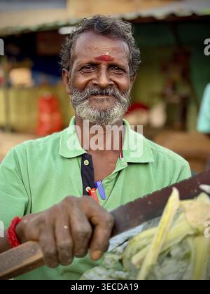 Ein lächelnder Mann mit Bart in grünem Hemd auf einem Markt in Indien Stockfoto