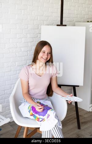 Eine junge, lächelnde Künstlerin, die eine Farbpalette und einen Pinsel in ihrem Atelier hält Stockfoto