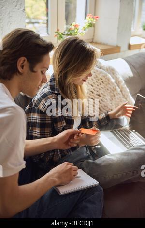Junge Paare, die beim Online-Shopping auf einem Laptop zu Hause eine Zahlungskarte wählen. Stockfoto