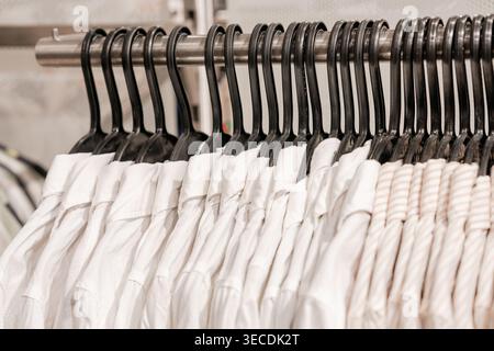 Weiße Hemden, die ordentlich auf Kleiderbügeln angeordnet sind. Minimalistisches Design und sauberes Garderobenkonzept. Neutrale Bekleidungspalette auf dem Rack. Moderner Stil und einfaches Wohnen. Stockfoto