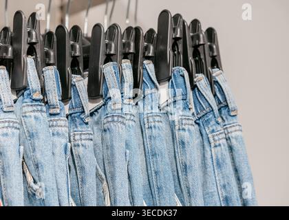 Denim-Overalls hängen am Regal im Laden. Ausstellungskonzept für Mode- und Einzelhandelsbekleidung für Kinder. Reihe blauer Denim-Overalls auf Kleiderbügeln. Lässiger Stil und Stockfoto