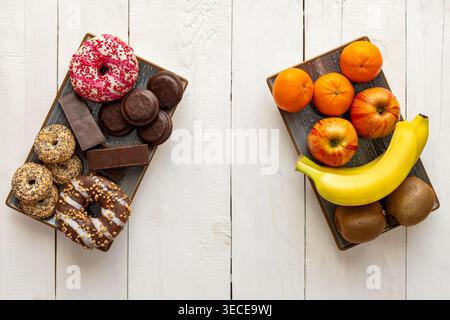 Gesundes Obst Versus Zuckerhaltige Snacks. Draufsicht auf frisches Obst und süße Desserts auf separaten Tellern, die gesunde Ernährung im Vergleich zu Junk Food zeigen Stockfoto