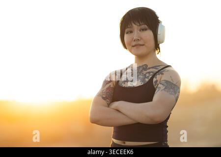 Junge asiatische Frau mit Kopfhörern und Tattoos, die selbstbewusst stehen Stockfoto