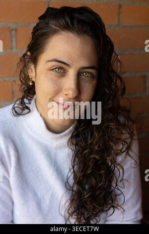 Frau mit grünen Augen und Sommersprossen lächelnd, posiert gegen eine Ziegelmauer Stockfoto