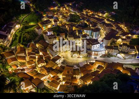 Blick aus der Vogelperspektive auf die beleuchtete historische Stadt Cudillero bei Nacht mit ihren charakteristischen roten Ziegeldächern und leuchtenden Straßen in den Hügeln Stockfoto