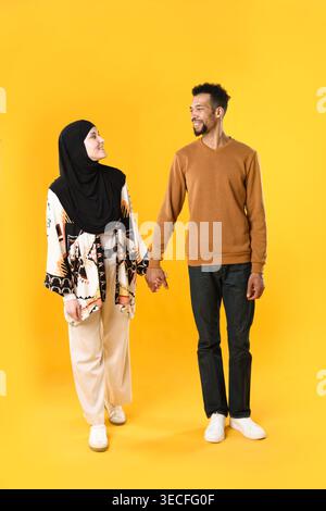 Glückliches muslimisches Paar, das Hände auf gelbem Hintergrund hält Stockfoto