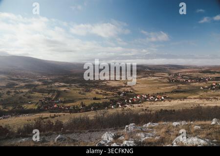Großer Panoramablick auf die ländliche Landschaft mit kleinem Dorf, sanften Hügeln und fernen Bergen. Stockfoto