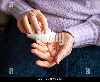 Ältere Frau, die eine Vitaminkapsel aus einer Flasche mit Händen, Medikamenten und häuslicher Pflege nimmt Stockfoto