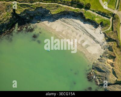 Blick aus der Vogelperspektive auf einen abgelegenen Sandstrand, eingebettet zwischen felsigen Klippen mit einem Paddelboarder im türkisfarbenen Wasser und Menschen, die sich am Ufer in WIC entspannen Stockfoto