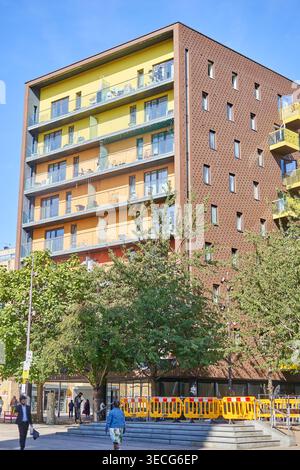 Ein modernes mehrstöckiges Wohnapartmentgebäude mit farbenfrohen gelben und orangefarbenen Fassaden und Glasbalkonen steht vor einem klaren blauen Himmel in Stockfoto