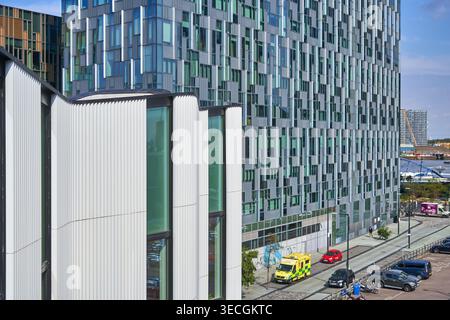 Moderne urbane Architektur in London mit einem Gebäude im Vordergrund, das durch eine charakteristische weiße vertikal geriffelte Verkleidung und große Glasfenster gekennzeichnet ist, Stockfoto