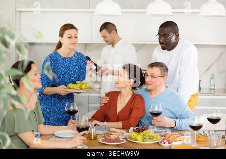 Glückliche Freunde mittleren Alters trinken Wein und unterhalten sich freundlich am Tisch Stockfoto