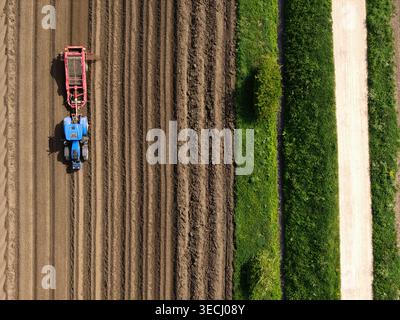 Aus der Vogelperspektive eines blauen Traktors, der ein braunes Feld neben einer grünen Hecke und einem unbefestigten Pfad in Knottingley, England, Vereinigtes Königreich, bebaut. Stockfoto