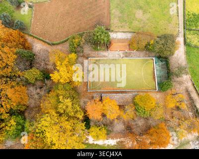 Blick aus der Vogelperspektive auf einen kleinen Fußballplatz, umgeben von lebhaften Herbstbäumen mit gelben und orangen Blättern in Alvoco das Varzeas, Coimbra, Portugal. Stockfoto