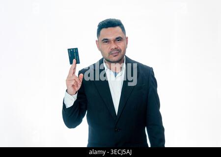 Ein professioneller indonesischer Mann in einem schwarzen Anzug, der eine Kreditkarte zwischen seinen Fingern hält, mit ernstem Gesichtsausdruck auf einem weißen Hintergrund. Stockfoto