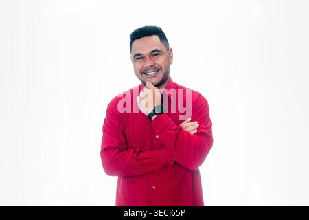 Porträt eines glücklichen Indonesiers in einem roten Hemd mit Hand am Kinn und verschränkten Armen, der Selbstvertrauen und Weisheit auf einem weißen Hintergrund ausstrahlt. Stockfoto