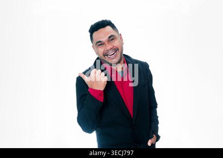 Porträt eines fröhlichen indonesischen Mannes in einem Anzug, der lacht und mit dem Daumen zur Seite zeigt, isoliert auf weißem Hintergrund. Stockfoto