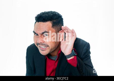 Porträt eines indonesischen Mannes in einem Anzug, der sein Ohr mit der Hand bedeckt, um aufmerksam zuzuhören, und mit konzentriertem Ausdruck in die Kamera schaut, isoliert auf Weiß. Stockfoto