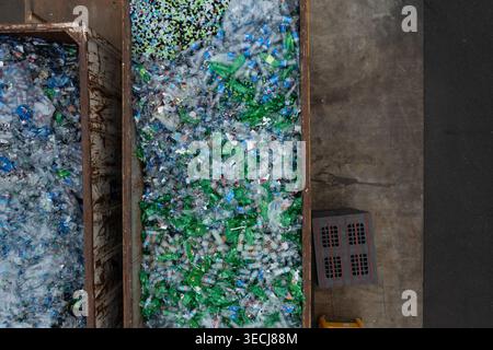 Aus der Vogelperspektive großer Metallbehälter, gefüllt mit grünen und durchsichtigen Kunststoffflaschen für das Recycling in einer Industrieanlage. Stockfoto