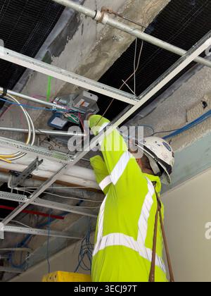 Elektriker, der Schaltkasten über der Decke auf der gewerblichen Baustelle installiert Stockfoto