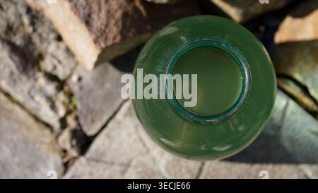 Ein Blick von oben auf ein großes grünes Glas gefüllt mit trüber Flüssigkeit, das draußen auf einer Steinoberfläche sitzt. Nahaufnahme Stockfoto
