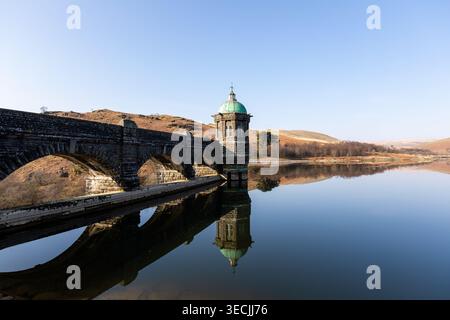 Craig Goch Dam im Elan Valley, Wales, mit einer viktorianischen Mauermauer und einem Kuppelventilturm, der sich bei Sonnenaufgang im ruhigen Reservoir spiegelt Stockfoto