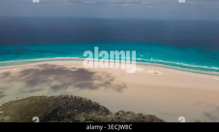 Aus der Vogelperspektive auf einen abgeschiedenen tropischen Strand mit weißem Sand, türkisfarbenem Meer, sanften Wellen und weichen Wolkenschatten unter einem bewölkten Himmel. Detwah Lagune, Stockfoto