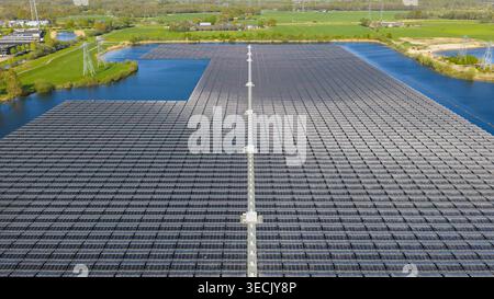 Aus der Vogelperspektive auf den schwimmenden Solarpark Sekdoornse Plas mit Tausenden von Photovoltaikanlagen auf einem See, der von grünen Feldern und Stromleitungen umgeben ist Stockfoto