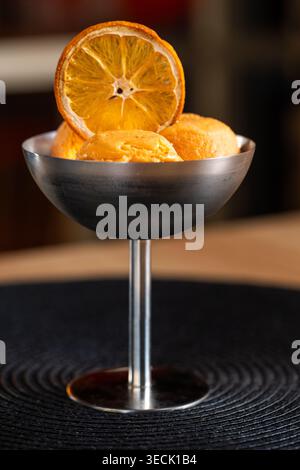 Orangensorbet in dunklem Metall-Coupé auf der Stängelseite Stockfoto