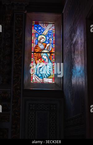 Religiöses Buntglasmotiv in der katholischen Kirche. Vertikales Foto mit niedriger Taste und Reflexionen und Kopierraum. Stockfoto