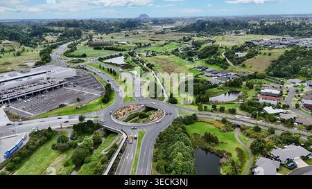 Drohnenansicht eines Kreisverkehrs mit einem Bach, der bei Tauranga Crossing in Tauriko, Neuseeland, mit dem Mount Maunganui in der Ba durchfließt Stockfoto