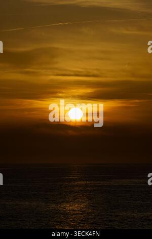 Goldener Sonnenuntergang über dem Mittelmeer, orangefarbener Himmel und Wolken, die sich auf ruhigem, dunklem Wasser spiegeln Stockfoto
