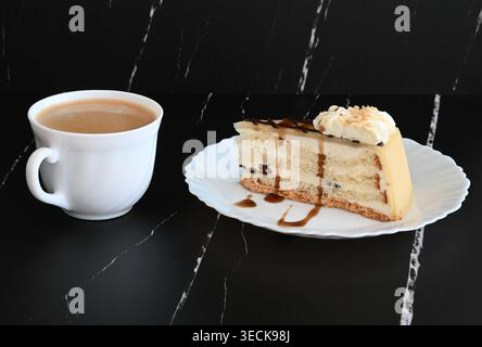 Ein Stück Kuchen auf einem weißen Teller und eine Tasse Kaffee vor dunklem Hintergrund Stockfoto