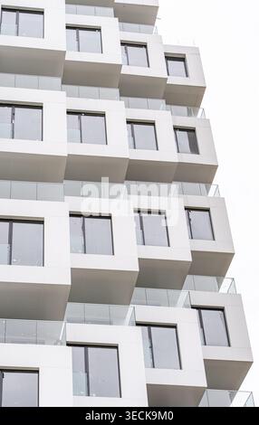 Nahaufnahme einer modernen Apartmentfassade mit gestapelten kubischen Balkonen, Betonkonstruktion, Glasgeländern und Metallrahmen, mit sauberer Geom Stockfoto
