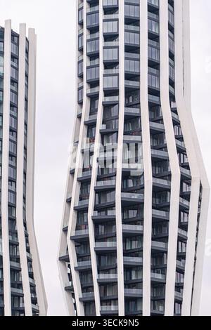 Abstrakte Ansicht eines modernen Hochhauses mit geschwungenen Betonflossen, dunklen Glasbalkonen und Metallrahmen, die eine elegante geometrische Fassade schaffen Stockfoto