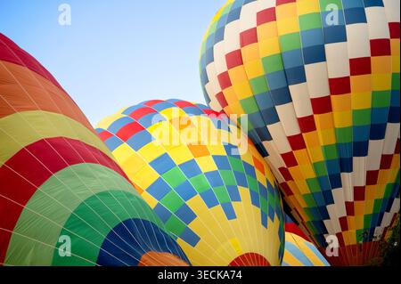 Drei bunte Heißluftballons steigen während eines sonnigen Fluges zusammen und zeigen lebendige Flickenteppiche und helle Stofftexturen in klarem Blau Stockfoto