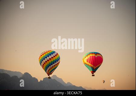 Bunte Heißluftballons schweben bei Sonnenaufgang in Vang Vieng, Laos, über der dramatischen Karstlandschaft und schaffen eine ruhige Reiseszene mit offenem Himmel und di Stockfoto