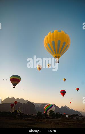 Bunte Heißluftballons treiben über den klaren Morgenhimmel über der Berglandschaft von Vang Vieng, Laos, und fangen das ruhige Abenteuer der Landschaft ein Stockfoto