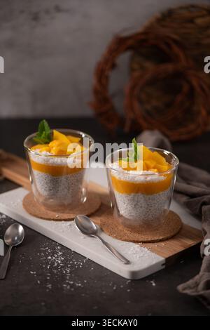 Zwei Gläser Chia-Samenpudding mit Mangopüree und frischen Fruchtstückchen. Sanfte natürliche Beleuchtung betont die cremige Textur und vibra Stockfoto