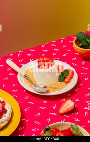 Ein entzückendes Panna Cotta Dessert garniert mit frischen Erdbeeren und Minzblättern, elegant auf einer strukturierten rosa Tischdecke, die eine lebendige Atmosphäre schafft Stockfoto