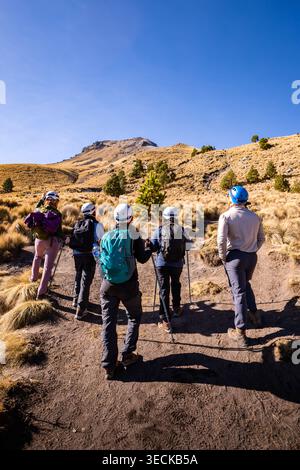 Gruppe von Wanderern mit Rucksäcken und Helmen, die bei Sonnenaufgang auf einem zerklüfteten Bergpfad bergauf wandern und einen Outdoor-Abenteuer-Aufstieg über trockene alpi genießen Stockfoto