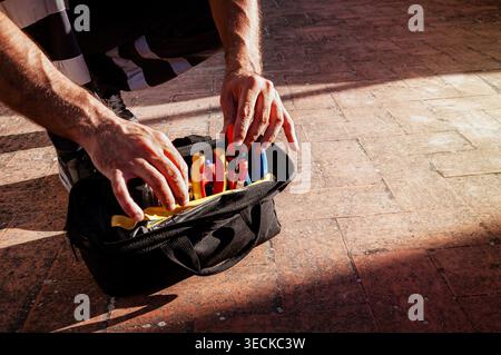 Nahaufnahme eines Technikers, der auf einem Fliesenboden kniet, Handwerkzeuge in einer offenen Werkzeugtasche für Wartungsarbeiten organisiert, wobei Arbeitssicherheit A hervorgehoben wird Stockfoto