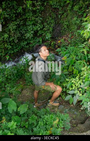 Erwachsener Mann, der einen steilen Pfad entlang eines kleinen Baches, umgeben von dichtem tropischem Grün im Botanischen Garten von Circasia, Antioquia, Kolumbien, auf einer na wandert Stockfoto