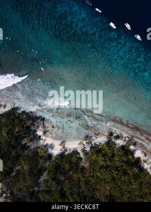Aus der Vogelperspektive auf eine tropische Insel der Malediven mit Palmenwald, felsiger Küste und türkisfarbenem Korallenriff. Kleines Boot und sanfte Surflinie klare Lagune wa Stockfoto