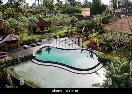 Erhöhter Blick auf ein tropisches Resort mit geschwungenem Swimmingpool, Liegestühlen, Villen und üppigem Palmengarten in Bali Tegagaland, Indonesien, eine ruhige trave Stockfoto