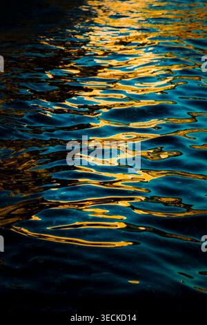 Abstrakte Nahaufnahme der rauschenden Wasseroberfläche mit lebhaften goldenen Reflexen und tiefen Blautönen, die eine schimmernde Textur und ein beruhigendes, luxuriöses AT schaffen Stockfoto